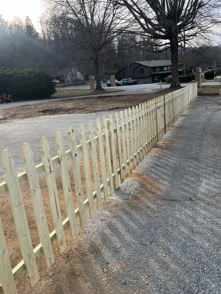 Freshly installed picket fence line along driveway edge