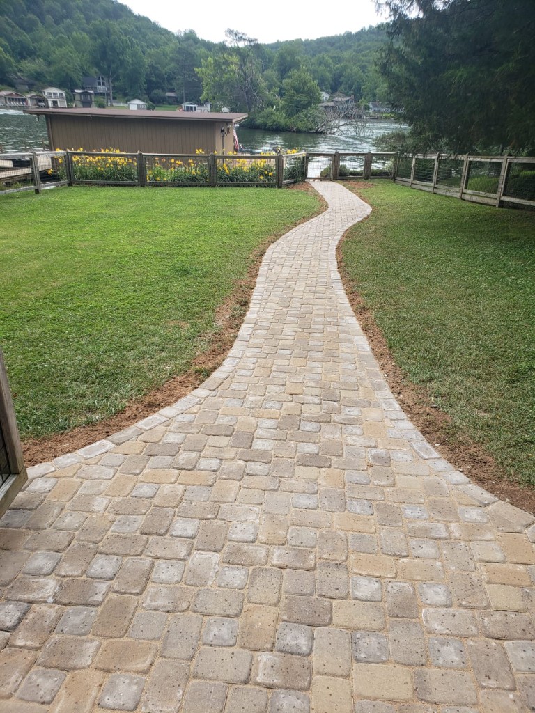 Curved paver walkway leading through lawn to a lakeside dock