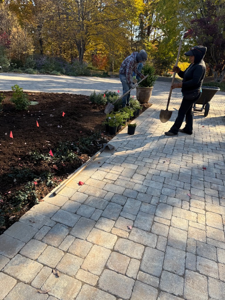 Crew installing planting bed edge detail beside paver patio